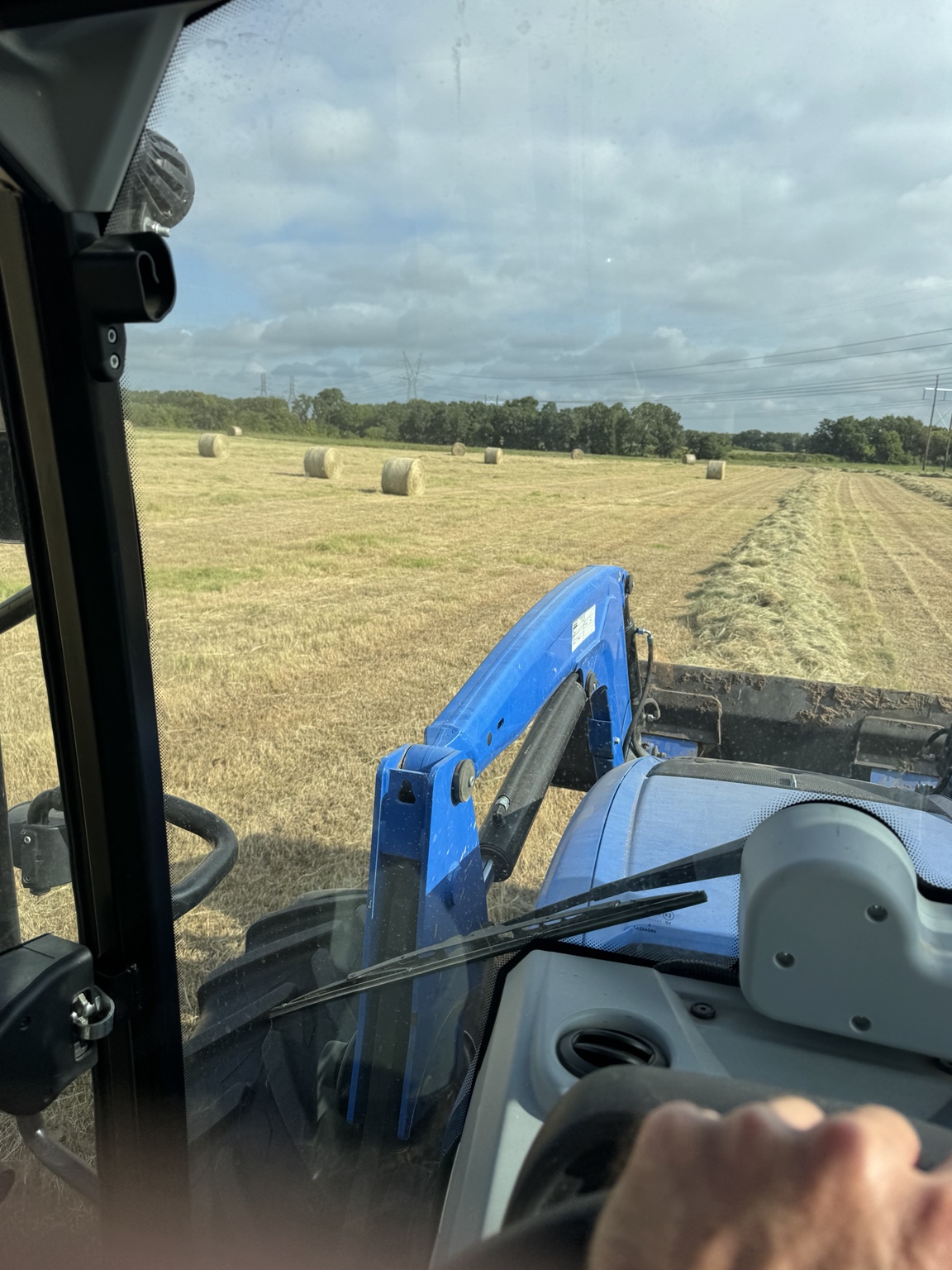 Hay windrow beside round bales seen from a tractor cab